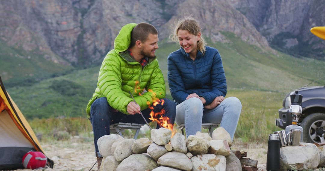Couple Enjoying Camping and Cooking by Fire in Mountain Field