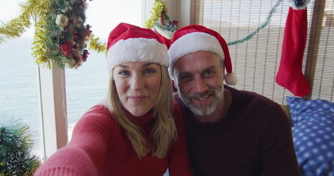 Happy Couple Enjoying Christmas at Home by the Sea Wearing Santa Hats - Free Images, Stock Photos and Pictures on Pikwizard.com