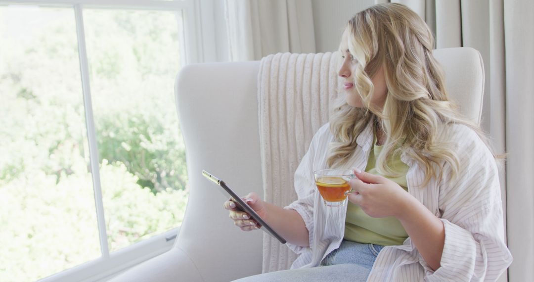 Young Woman Relaxing with Tablet and Tea by Window - Free Images, Stock Photos and Pictures on Pikwizard.com