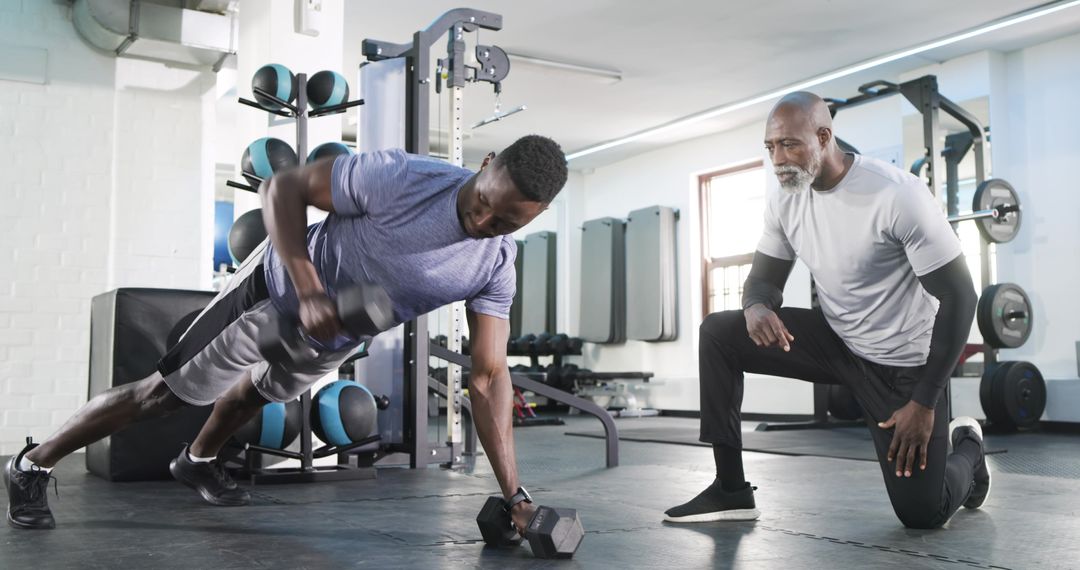 Trainer Guiding Client in Dumbbell Renegade Row at Gym
