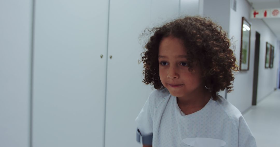 Young child with curly hair in hospital corridor wearing medical gown - Free Images, Stock Photos and Pictures on Pikwizard.com