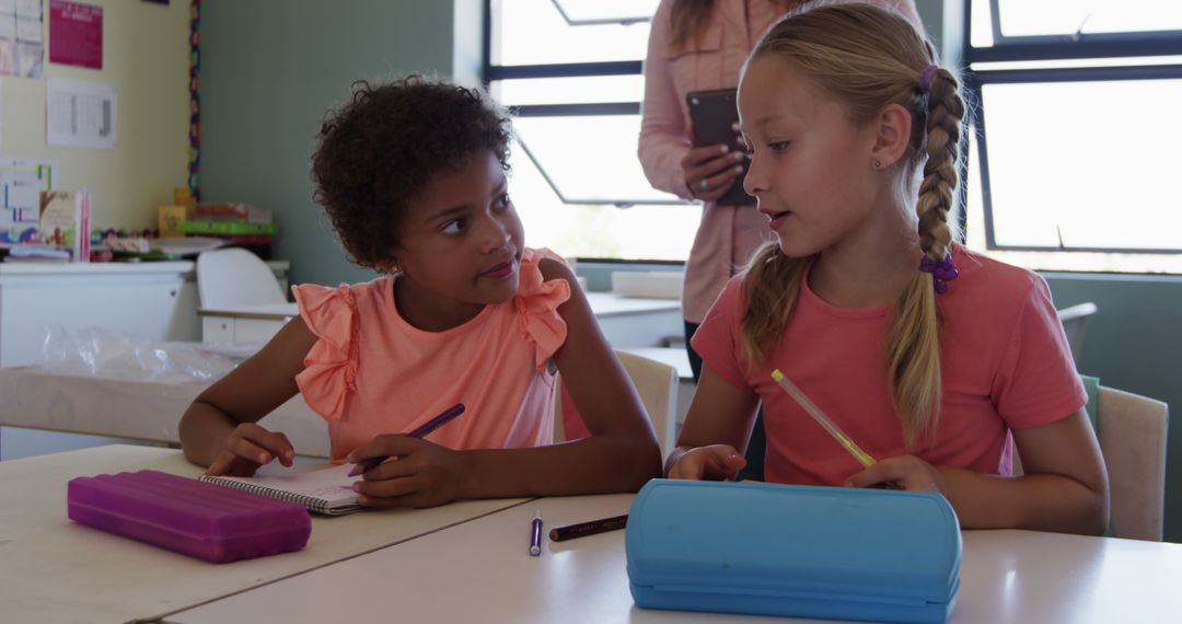 Diverse Girls Interacting in Classroom with Teacher in Background