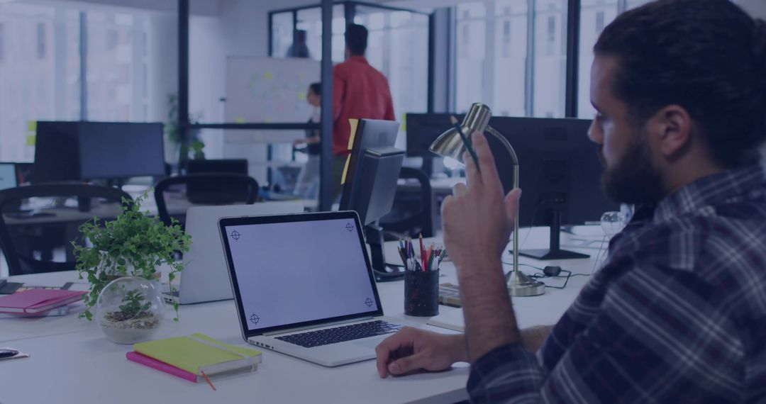 Bearded man reaching and adjusting brass desk lamp while working at modern open-plan office