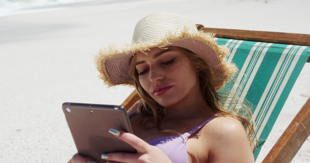 Young woman relaxing on beach sunbed reading tablet - Free Images, Stock Photos and Pictures on Pikwizard.com