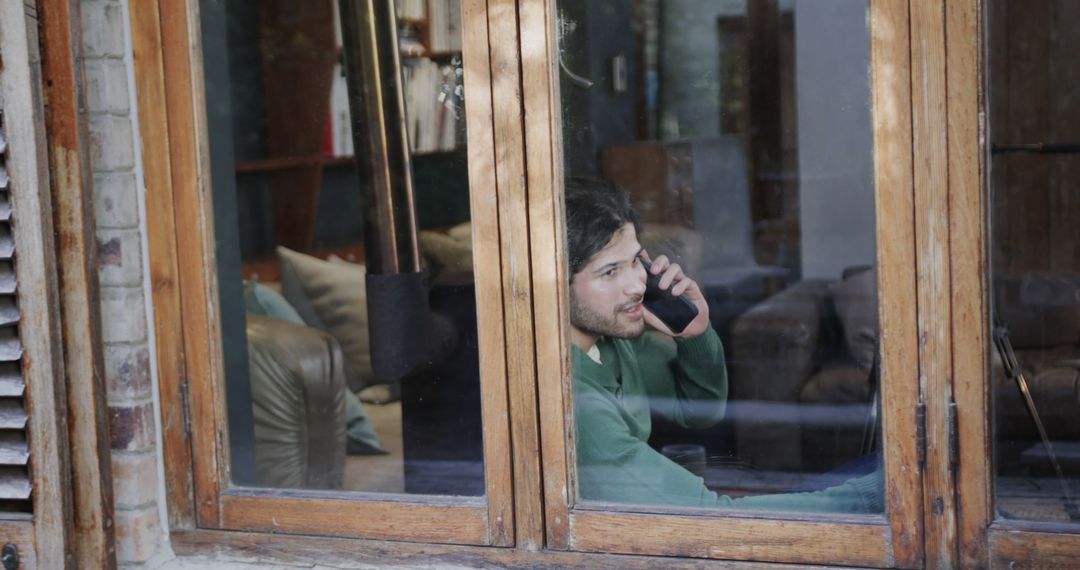 Young Man Talking on Smartphone Next to Window in Cozy Home - Free Images, Stock Photos and Pictures on Pikwizard.com