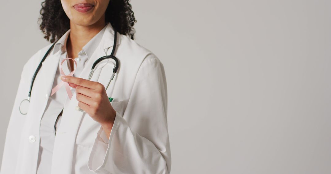 Image of smiling biracial female doctor holding pink breast cancer ribbon - Free Images, Stock Photos and Pictures on Pikwizard.com