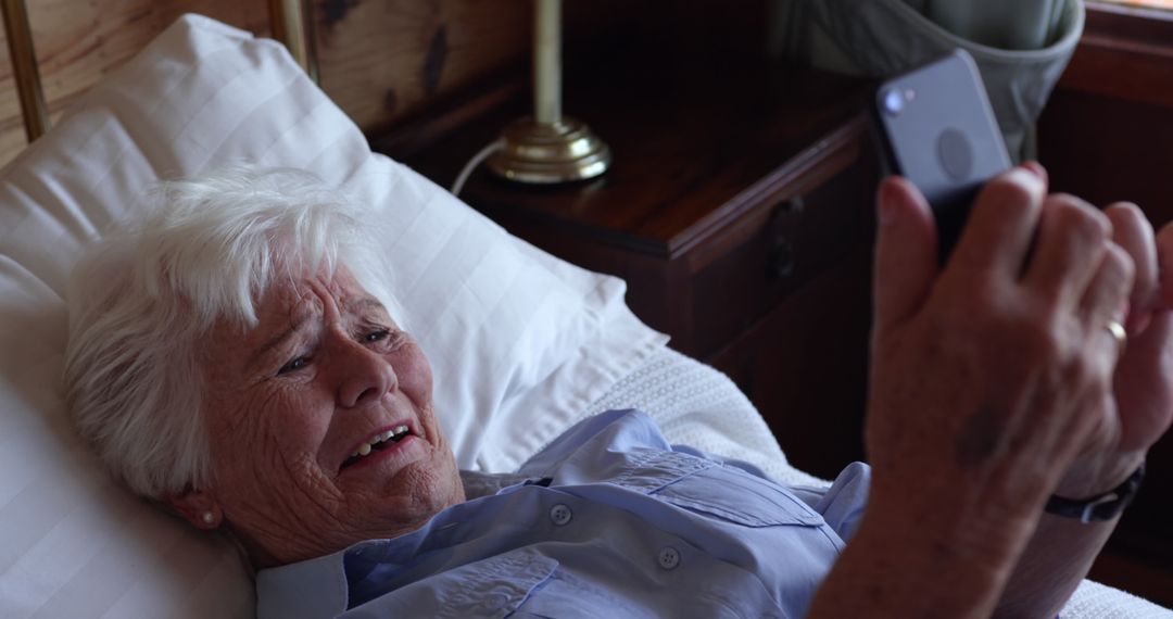 Senior Woman Lying in Bed Looking Distressed While Using Smartphone