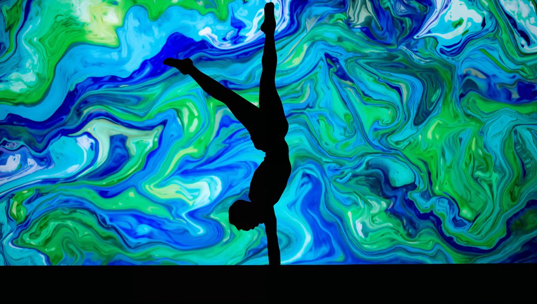 Silhouette Acrobat Performing One-Arm Handstand on Stage with Vibrant Marbled Projection