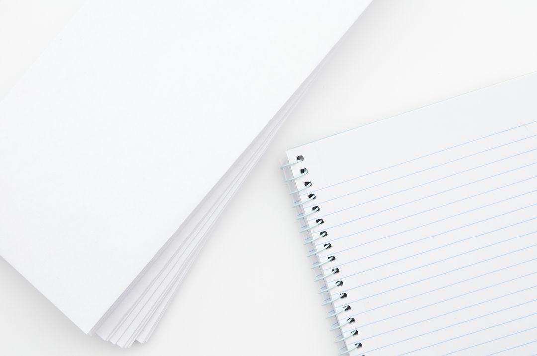 White Paper and Blue-Lined Spiral Notebook on Blank Surface