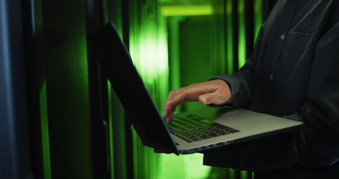 IT Technician Working on Laptop in Data Center with Green Lighting - Free Images, Stock Photos and Pictures on Pikwizard.com