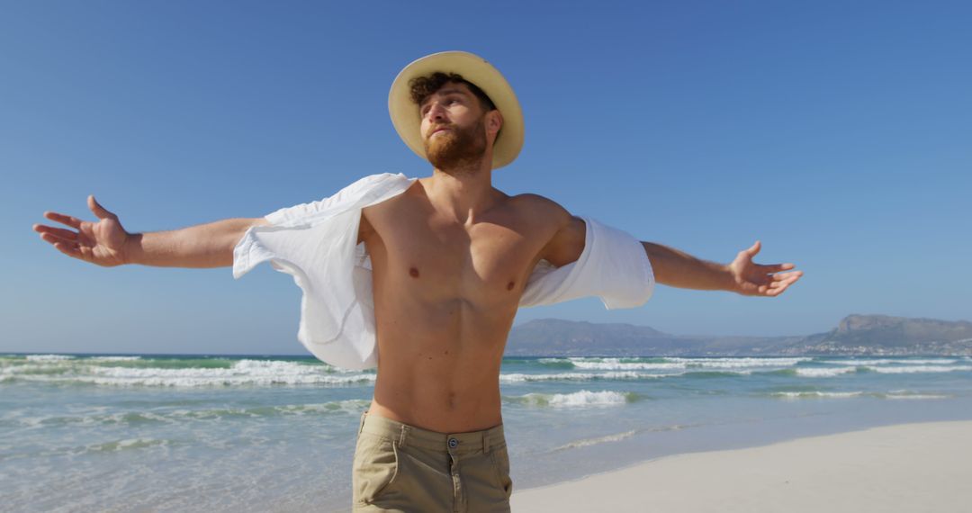 Young Man Enjoying Sunny Day at Beach with Arms Outstretched - Free Images, Stock Photos and Pictures on Pikwizard.com