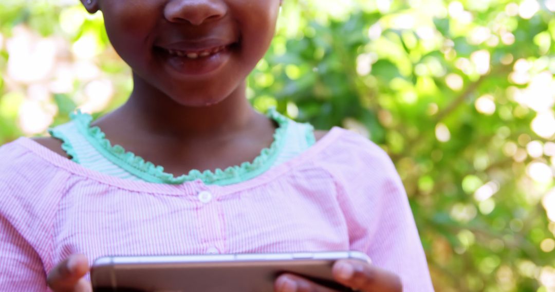 Smiling Young Girl Using Tablet Outdoors in Sunny Garden - Free Images, Stock Photos and Pictures on Pikwizard.com