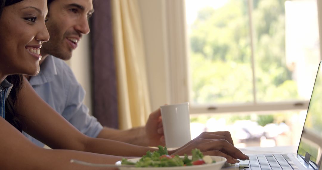 Couple Enjoying Meal and Browsing Laptop at Home