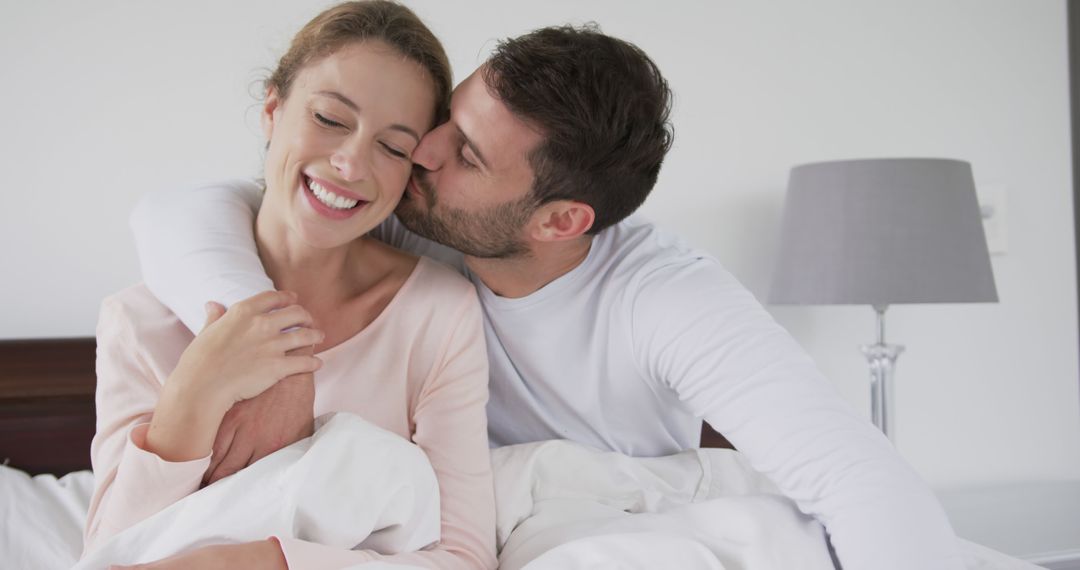 Happy caucasian couple wearing pyjamas kissing and embracing on bed at home - Free Images, Stock Photos and Pictures on Pikwizard.com