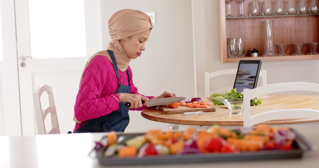 Woman in Hijab Following Recipe on Tablet, Cutting Vegetables - Free Images, Stock Photos and Pictures on Pikwizard.com