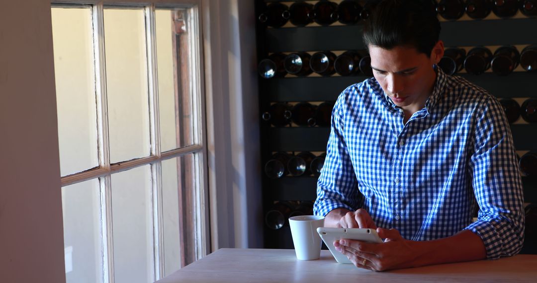 Man Enjoying Digital Tablet in Wine Cellar with Coffee Mug - Free Images, Stock Photos and Pictures on Pikwizard.com