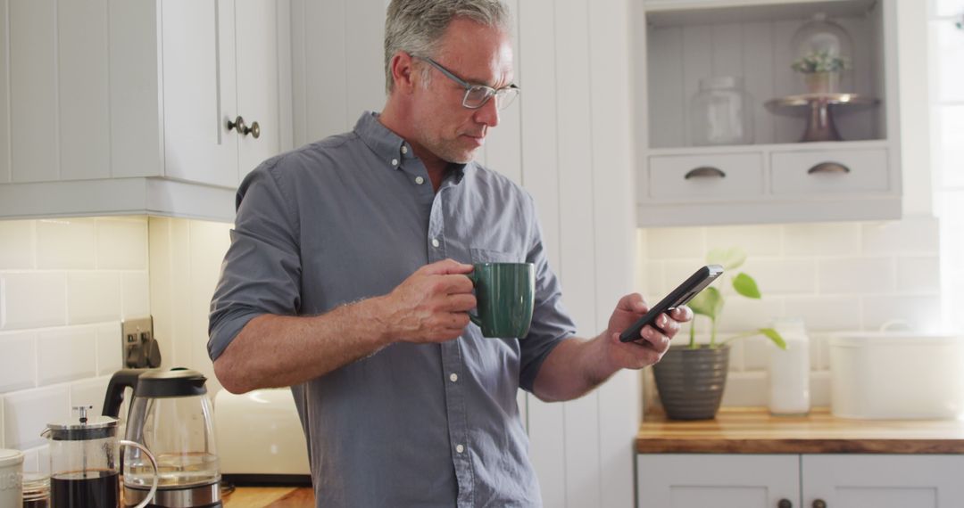 Middle-aged man drinking coffee and using smartphone in modern kitchen - Free Images, Stock Photos and Pictures on Pikwizard.com