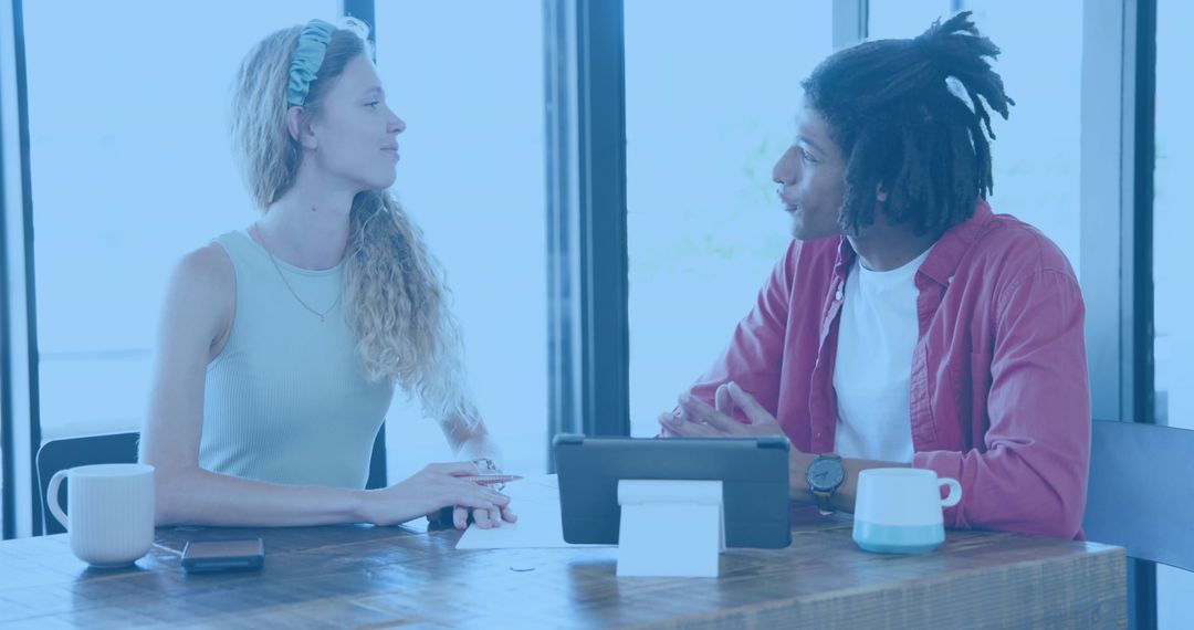 Young colleagues discussing project over tablet at sunlit cafe workspace