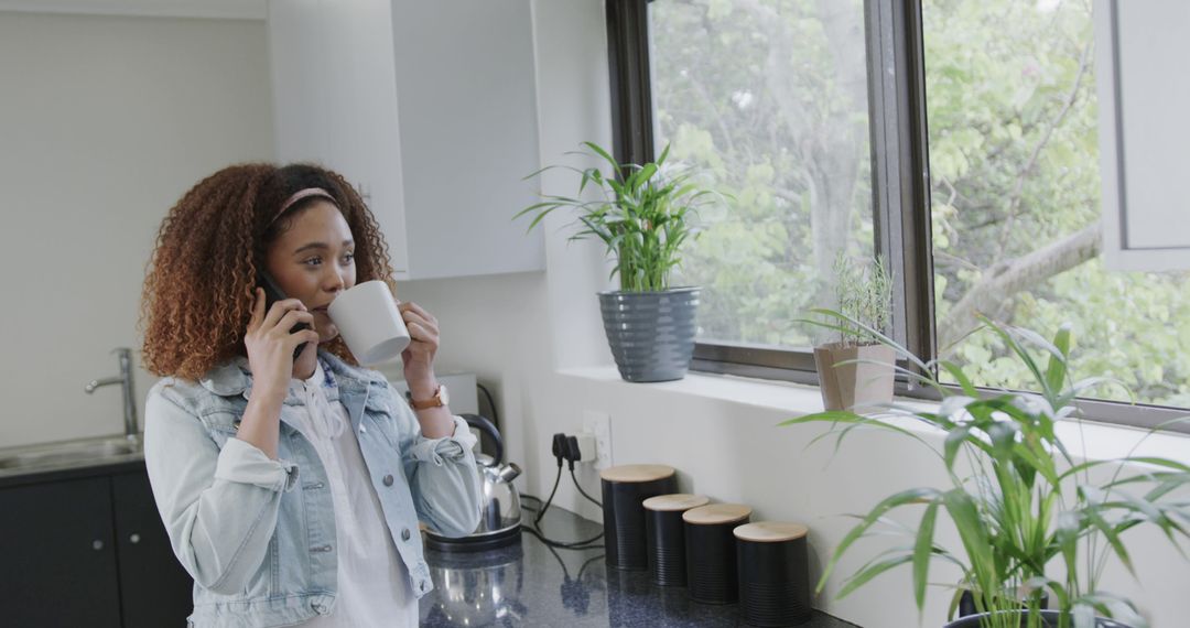 Young African American Woman Talking on Phone and Drinking Coffee in Modern Kitchen - Free Images, Stock Photos and Pictures on Pikwizard.com