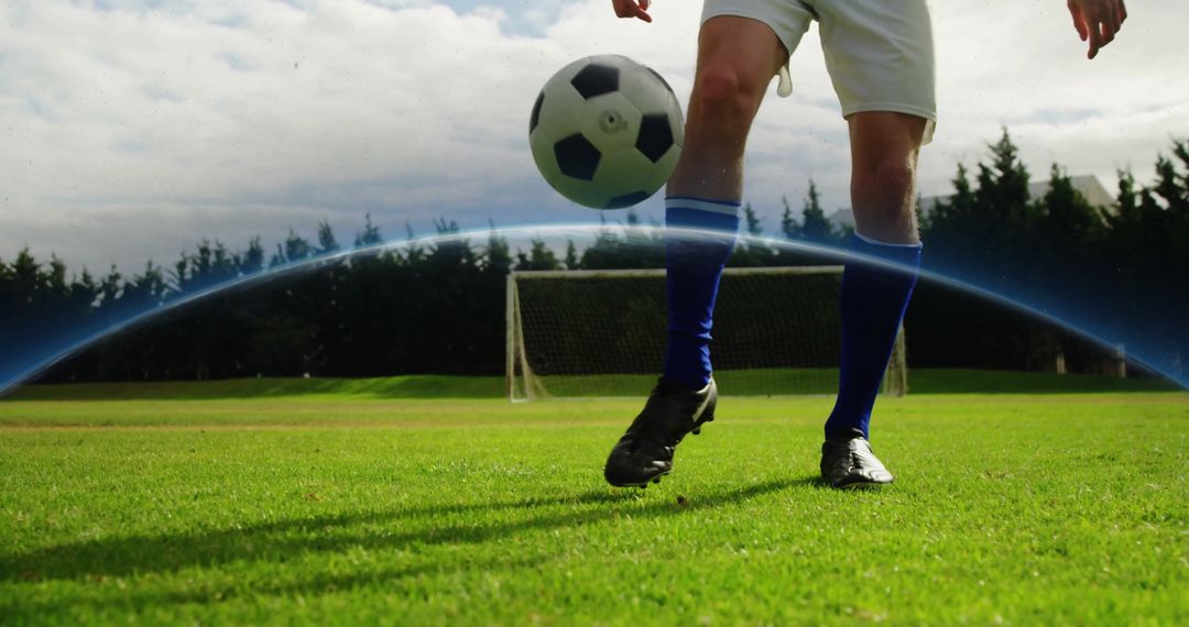 Football Player Juggling Soccer Ball on Grassy Field Against Goalpost