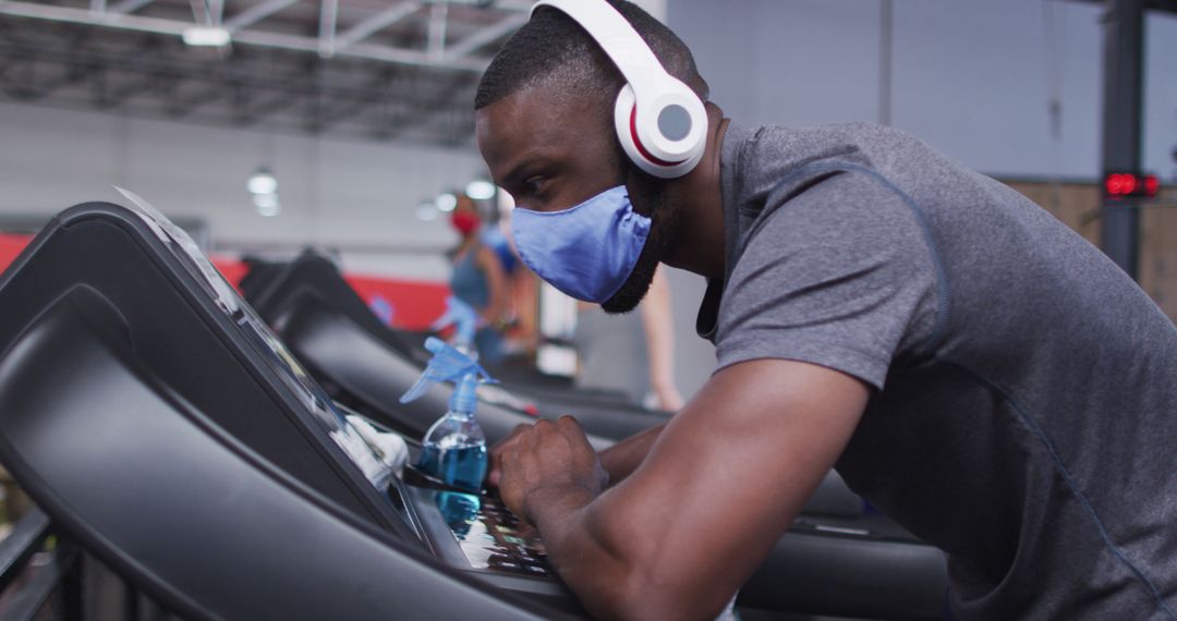 Exhausted African American man in mask and headphones rests on a treadmill amid COVID-19. - Free Images, Stock Photos and Pictures on Pikwizard.com