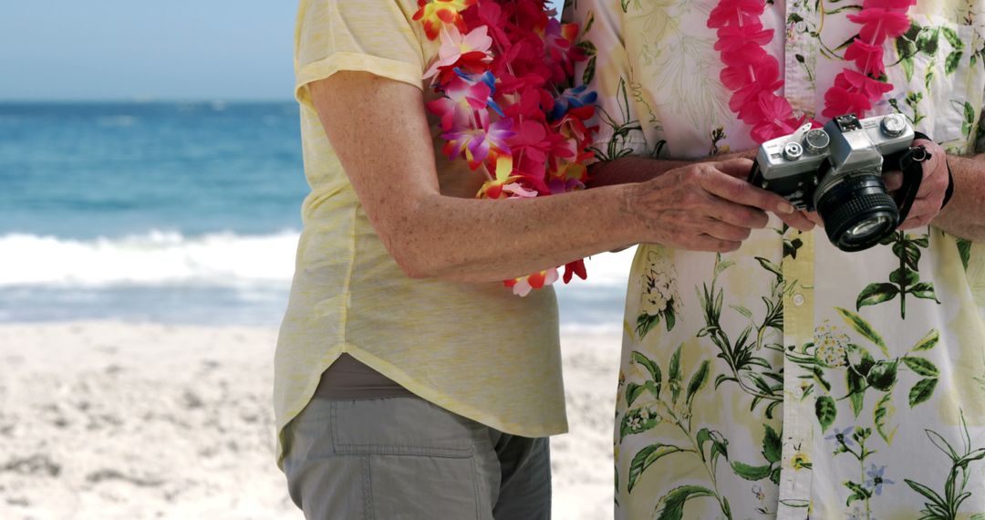 Senior Couple Enjoying Beach Vacation with Camera and Leis - Free Images, Stock Photos and Pictures on Pikwizard.com