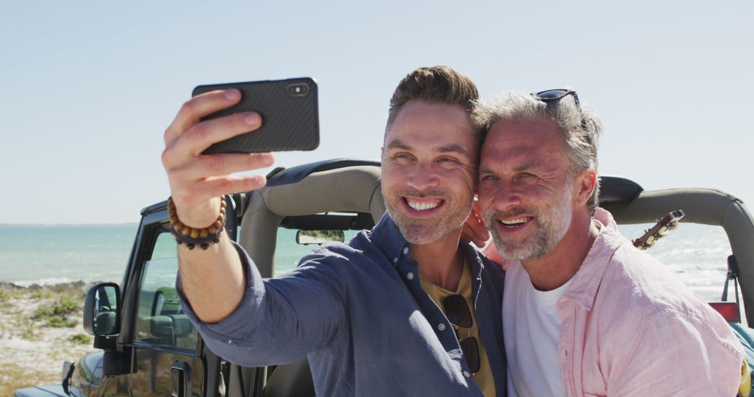 Happy caucasian gay male couple taking selfies and smiling by car on sunny day at the beach - Free Images, Stock Photos and Pictures on Pikwizard.com