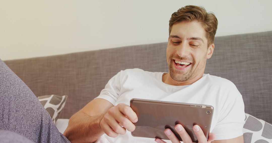 Young Man Laughing While Using Tablet on Couch - Free Images, Stock Photos and Pictures on Pikwizard.com