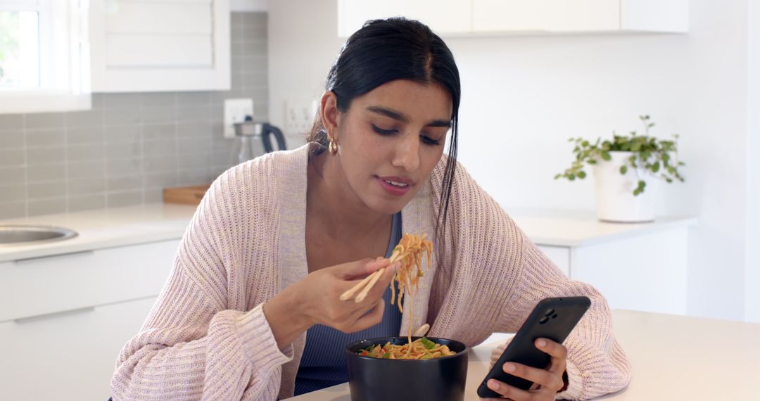 Woman Enjoying Noodles at Home While Checking Smartphone