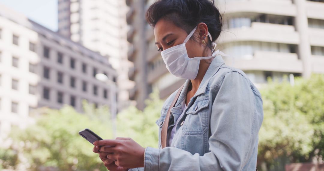 Woman in Denim Jacket Wearing Face Mask Using Smartphone Outdoors - Free Images, Stock Photos and Pictures on Pikwizard.com