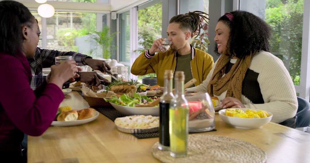 Friends Sharing Roast Dinner Around Sunlit Modern Table With Salad and Corn