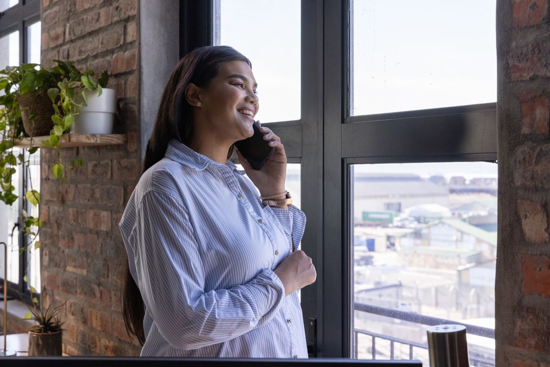 Pregnant Woman in Loft Office Smiling While on Call by Window