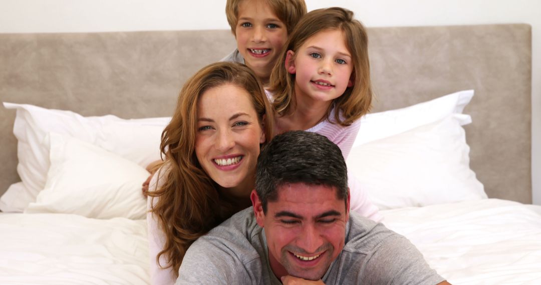 Happy Family of Four Relaxing on Bed Smiling Together - Free Images, Stock Photos and Pictures on Pikwizard.com