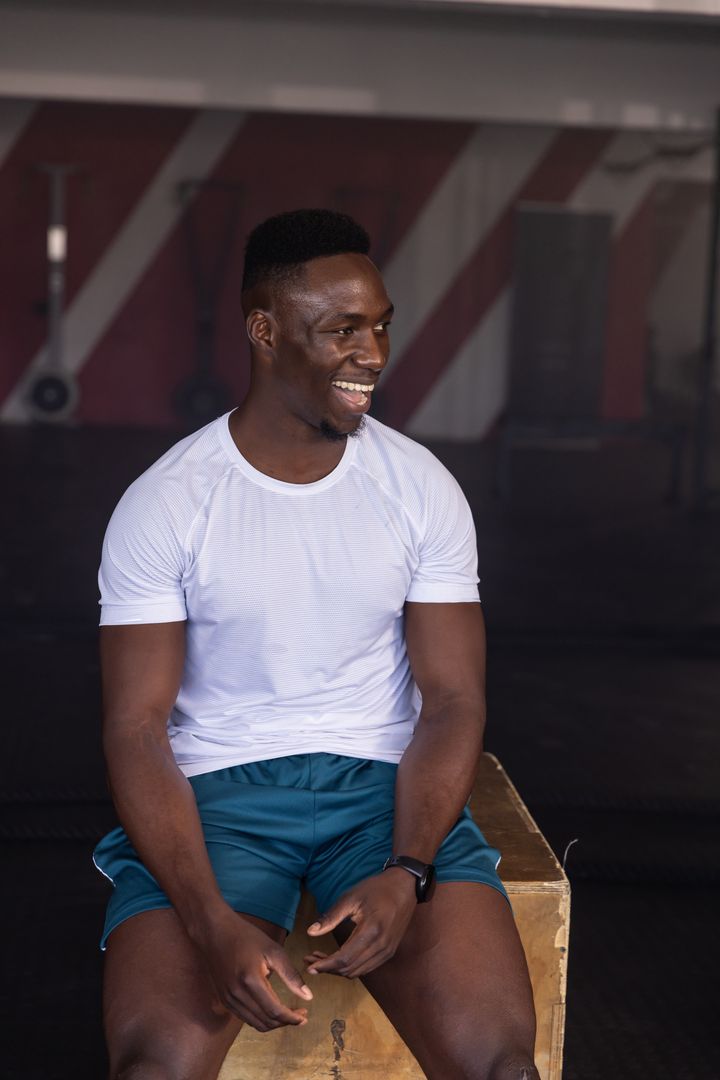Athletic Man Resting on Box in Gym with Fitness Tracker