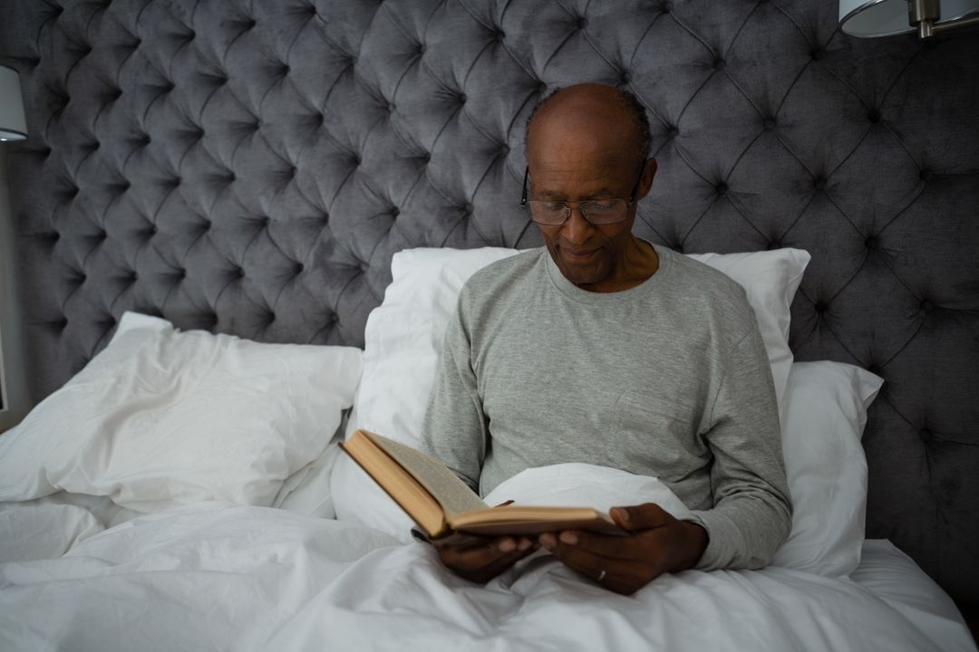 Senior man reading book while sitting on bed - Free Images, Stock Photos and Pictures on Pikwizard.com