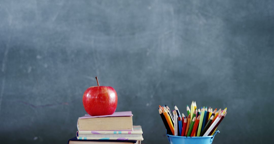 Apple on Books with Pencils Against Blackboard Backdrop