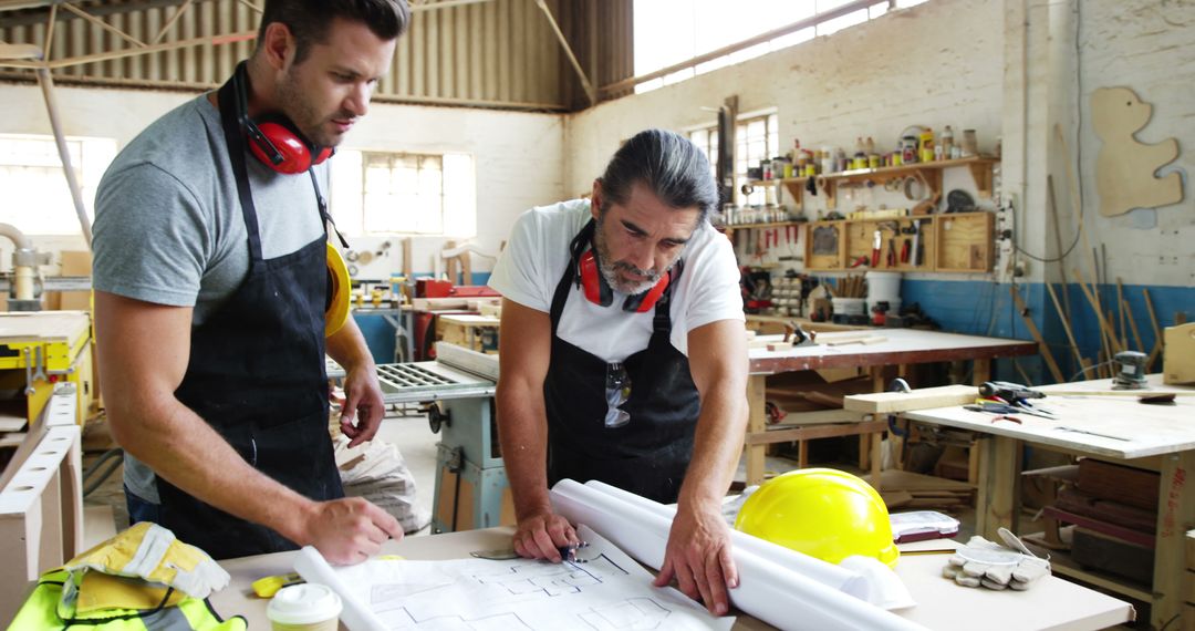 Two Male Carpentry Workers Reviewing Building Plans in Workshop - Free Images, Stock Photos and Pictures on Pikwizard.com