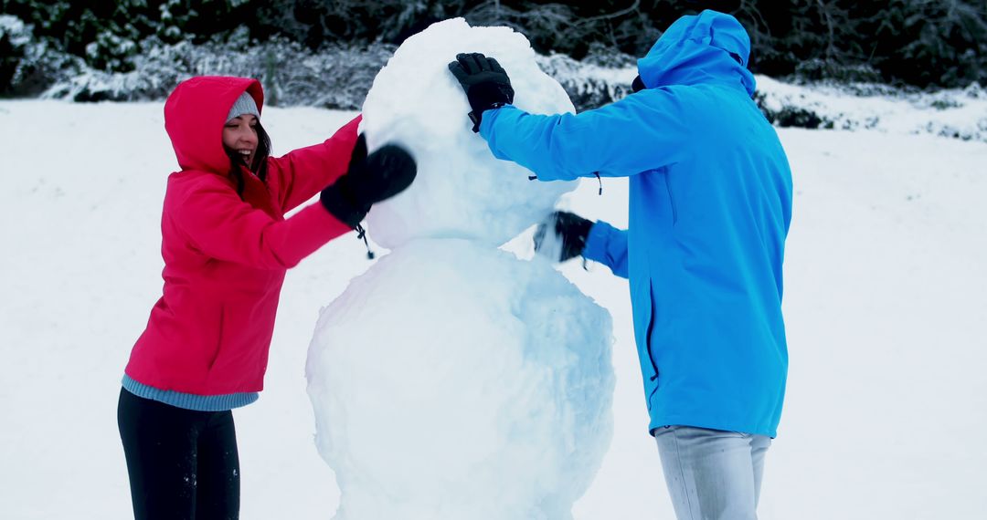 Couple building snowman together in winter park - Free Images, Stock Photos and Pictures on Pikwizard.com