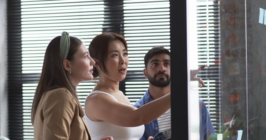 Collaborative Team Discussing Ideas at Glass Board in Office