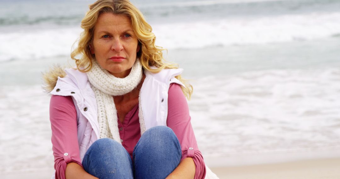 Pensive Middle-Aged Woman Sitting by Ocean on Overcast Day - Free Images, Stock Photos and Pictures on Pikwizard.com