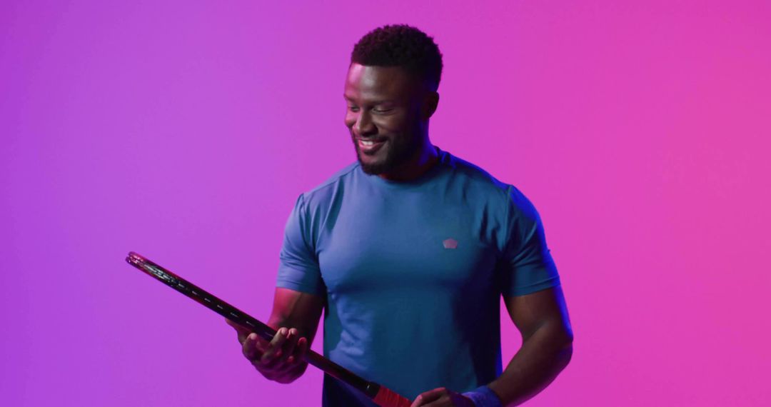 Athlete Examining Tennis Racket in Neon Studio Lighting