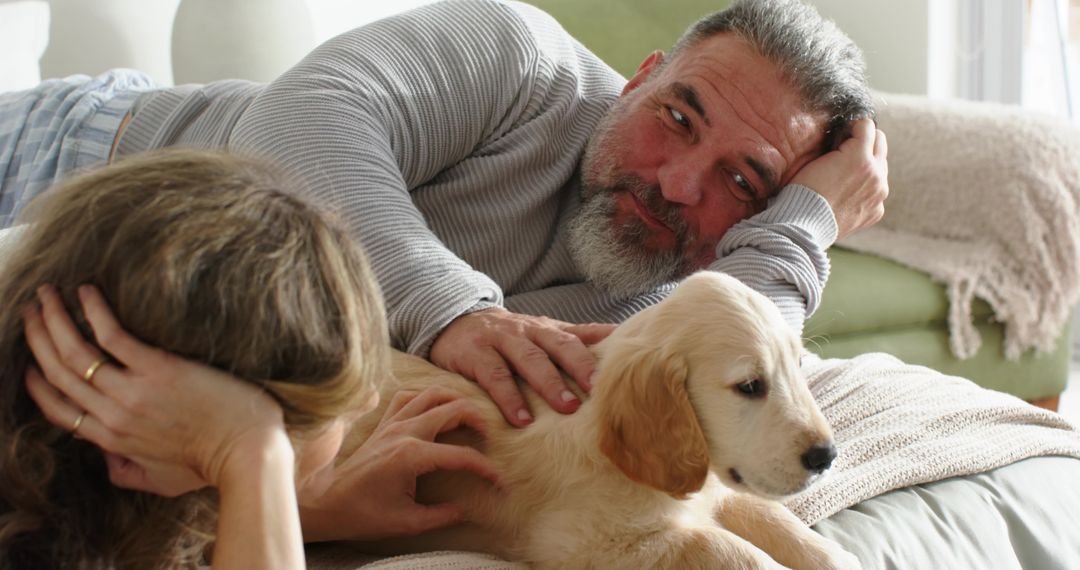 Mature couple relaxing and petting golden retriever puppy on cozy sofa at home