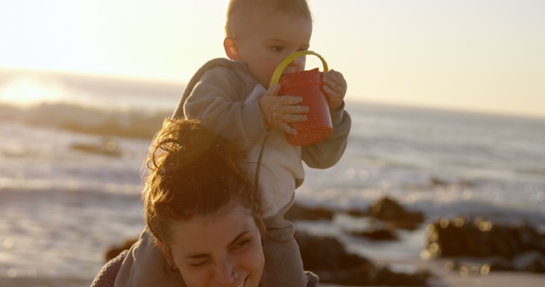 Mother carrying baby on shoulders at beach during sunset - Free Images, Stock Photos and Pictures on Pikwizard.com