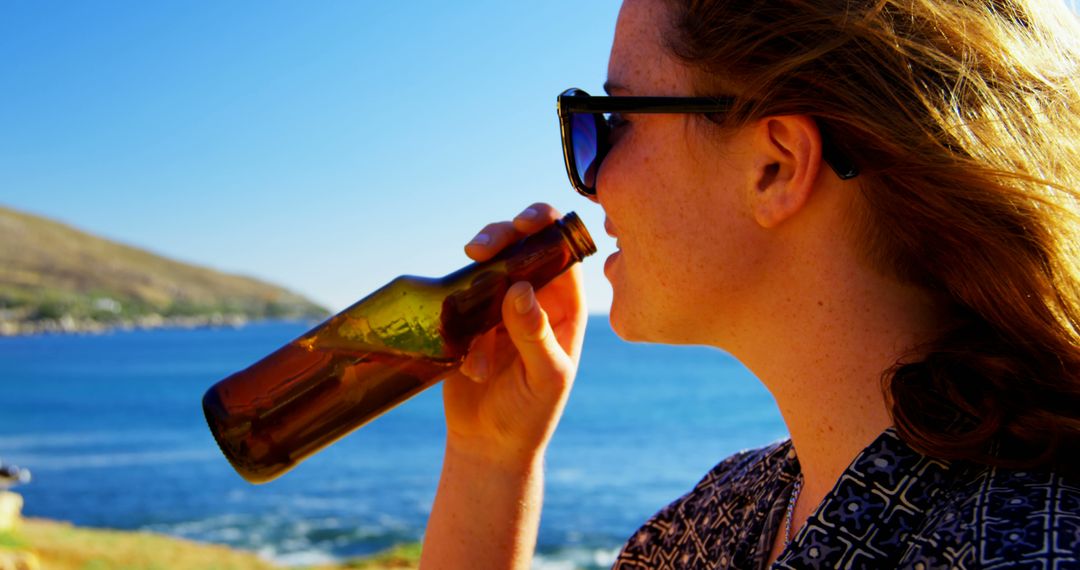 Young Woman Drinking Beer by the Sea on Sunny Day - Free Images, Stock Photos and Pictures on Pikwizard.com