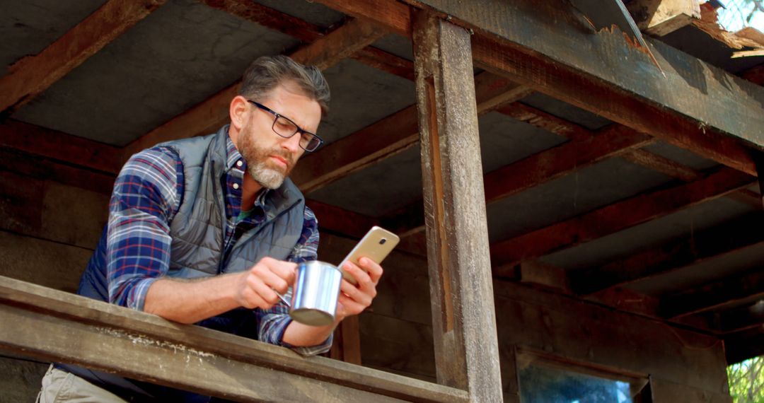 Man Enjoying Coffee on Rustic Cabin Porch While Using Smartphone - Free Images, Stock Photos and Pictures on Pikwizard.com