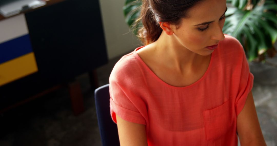 Focused Woman in Coral Shirt Working in Modern Office Environment - Free Images, Stock Photos and Pictures on Pikwizard.com