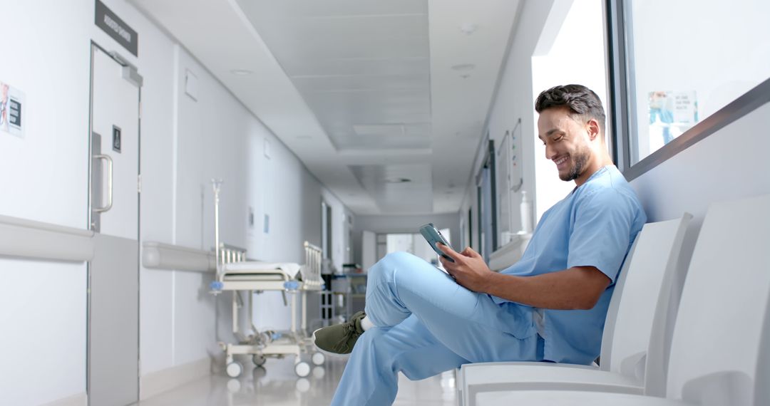 Smiling Male Nurse Sitting in Hospital Corridor Using Digital Tablet - Free Images, Stock Photos and Pictures on Pikwizard.com