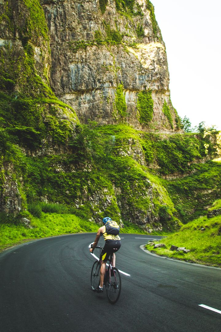 Cyclist Biking on Curved Mountain Road in Scenic Green Landscape - Free Images, Stock Photos and Pictures on Pikwizard.com