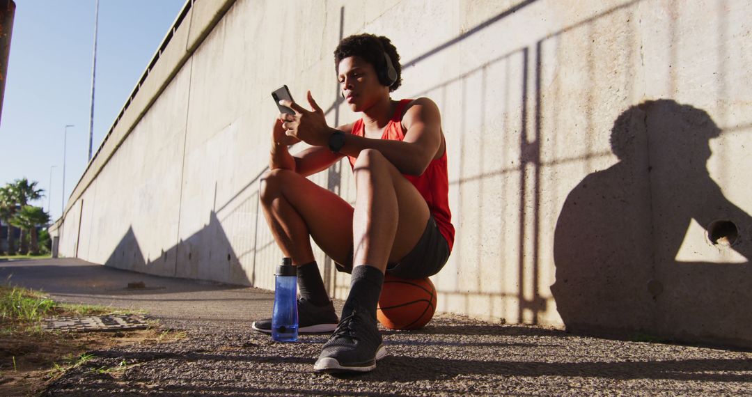 Athletic Man Relaxing with Smartphone and Basketball