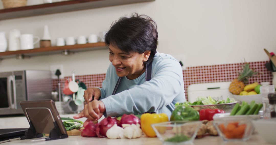 Middle-aged Asian woman cooking healthy meal in kitchen while using tablet - Free Images, Stock Photos and Pictures on Pikwizard.com